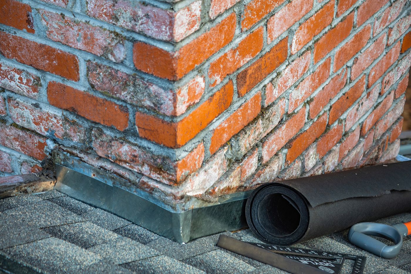 Metal flashing around a brick chimney where it meets asphalt shingles