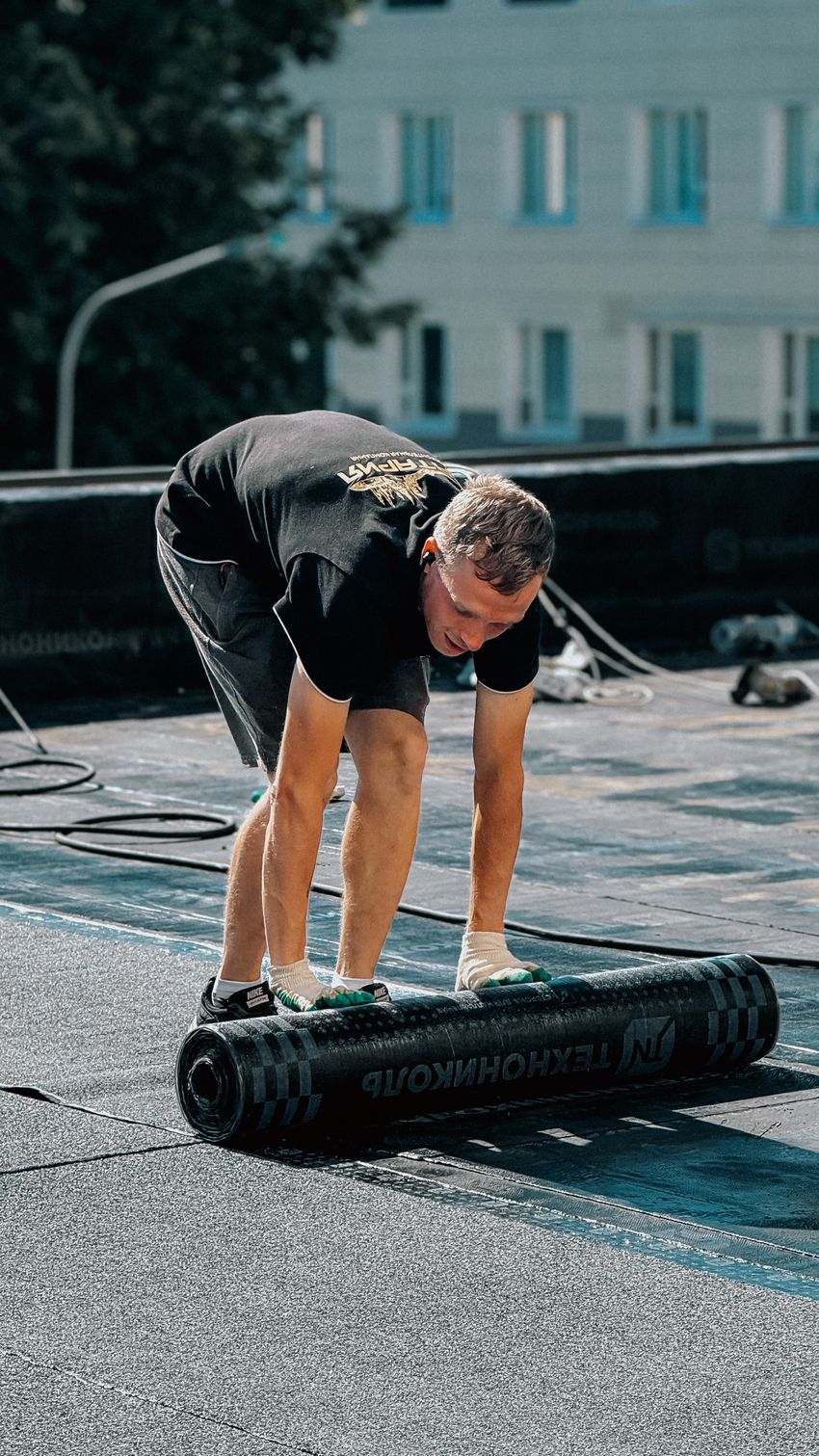 Worker laying a rolled bituminous waterproofing membrane on a flat roof