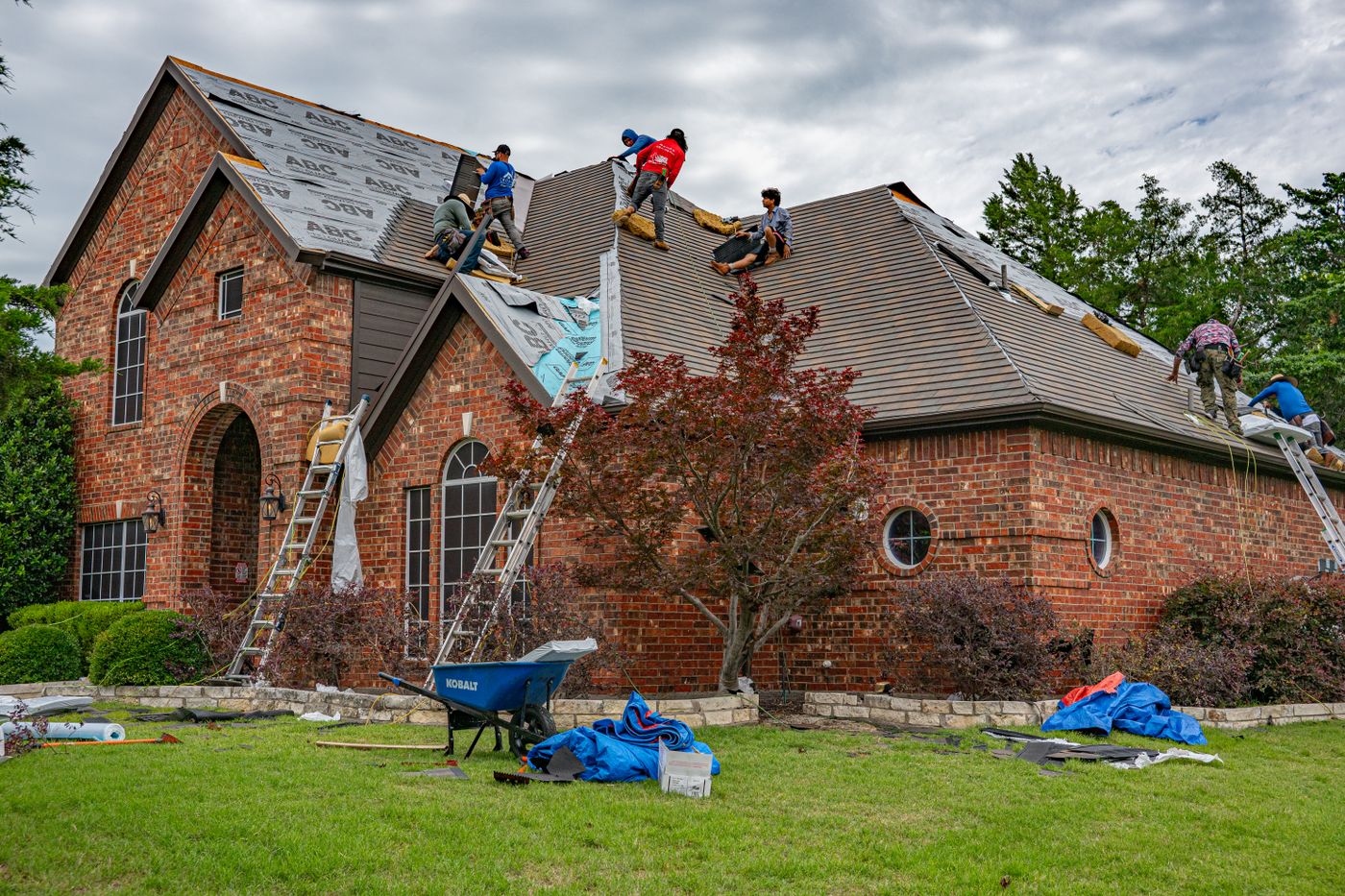 Roofing crew and ladders on a steep residential roof with multiple slopes