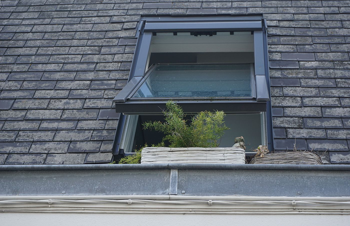 Open roof window showing metal flashing between the frame and surrounding roof tiles