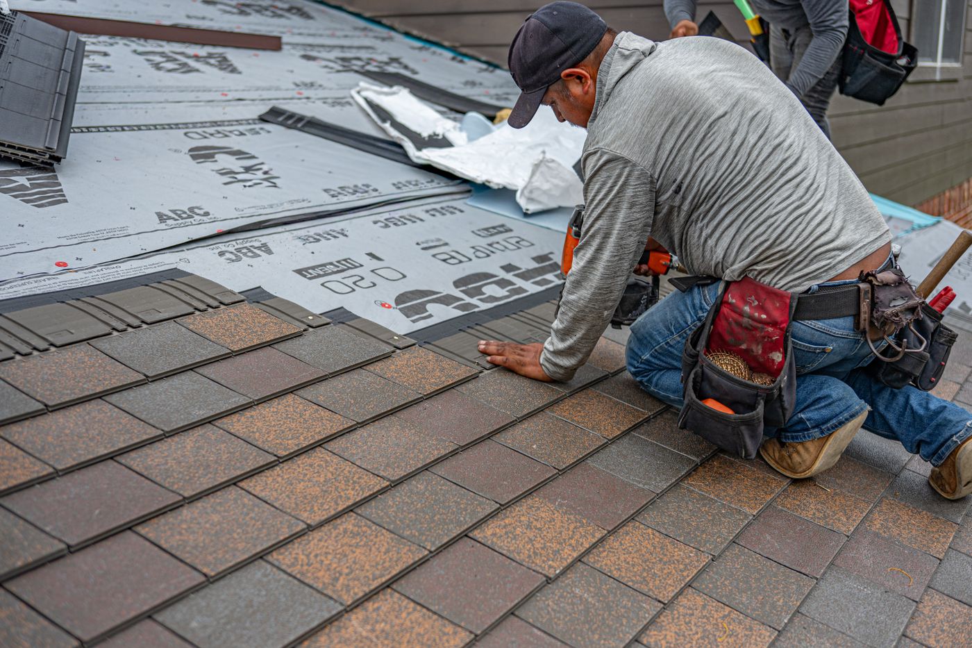 Roofer fastening asphalt shingles above roof underlayment