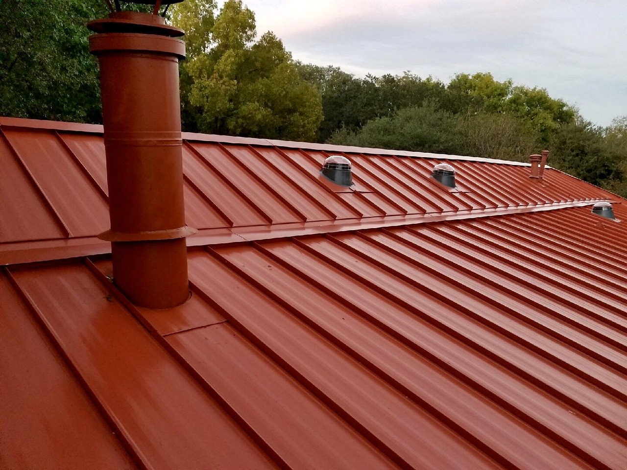 Standing-seam metal roof with raised panel seams and flashed pipe penetrations